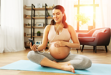 Image showing happy pregnant woman sitting on yoga mat at home