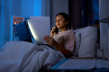 Image showing woman with papers calling on phone in bed at night