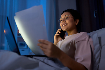 Image showing woman with papers calling on phone in bed at night