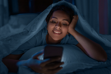 Image showing woman with smartphone under duvet in bed at night