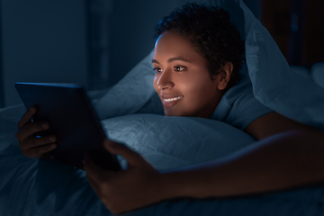 Image showing woman with tablet pc under duvet in bed at night