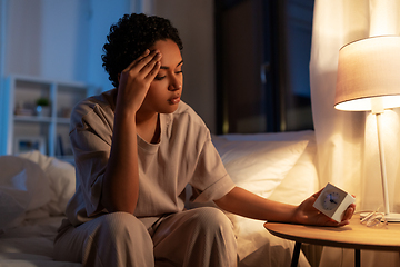 Image showing african woman with clock sitting on bed at night