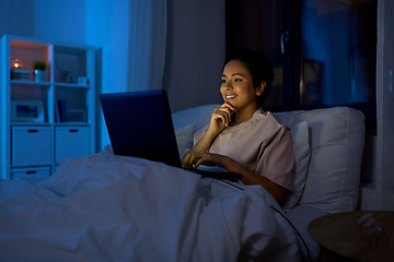 Image showing smiling woman with laptop in bed at home at night