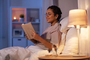 Image showing smiling young woman reading book in bed at home