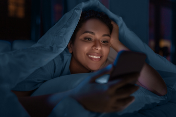 Image showing woman with smartphone under duvet in bed at night