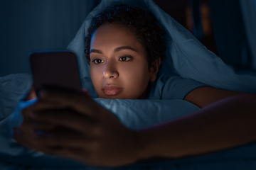 Image showing woman with smartphone under duvet in bed at night