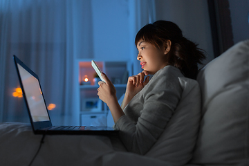 Image showing asian woman with smartphone in bed at night