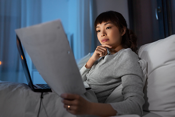 Image showing asian woman with laptop and papers in bed at night