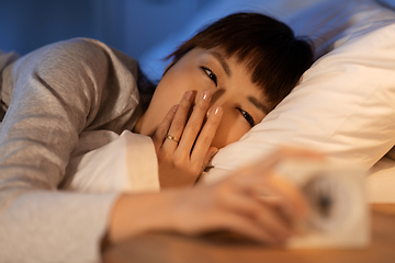 Image showing asian woman with clock yawning in bed at night