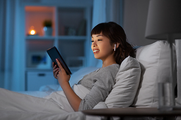 Image showing woman with tablet pc in earphones in bed at night