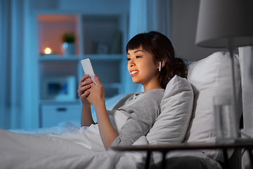 Image showing woman with phone and earphones in bed at night