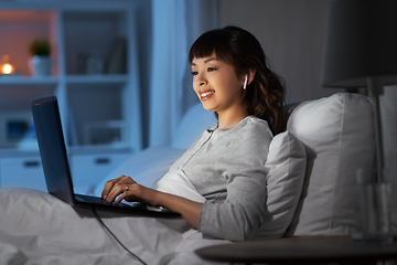 Image showing woman with laptop and earphones in bed at night