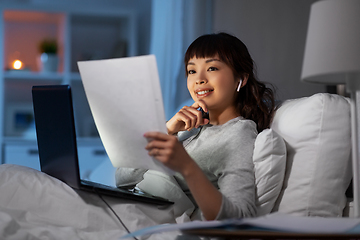 Image showing woman with laptop and papers in bed at night
