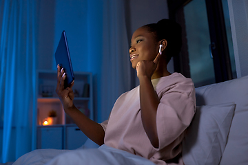 Image showing woman with tablet pc in earphones in bed at night