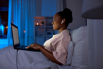 Image showing woman with laptop and earphones in bed at night