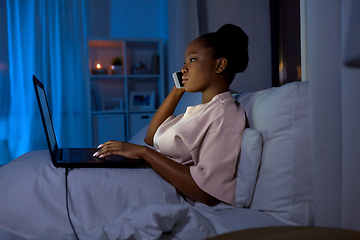 Image showing woman with laptop calling on phone in bed at night