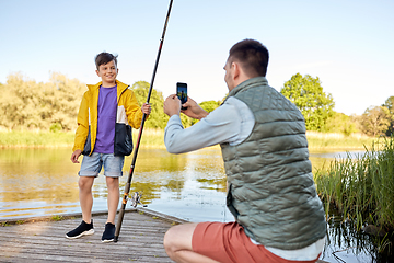 Image showing father photographing son with fishing rod on river