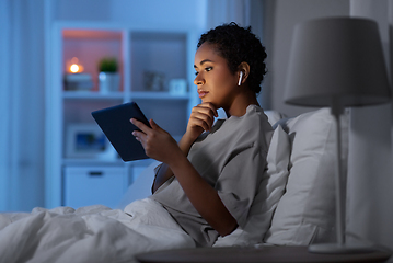 Image showing woman with tablet pc in earphones in bed at night