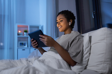 Image showing woman with tablet pc in earphones in bed at night