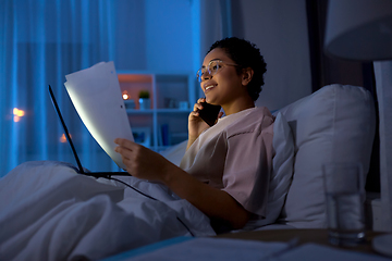 Image showing woman with papers calling on phone in bed at night