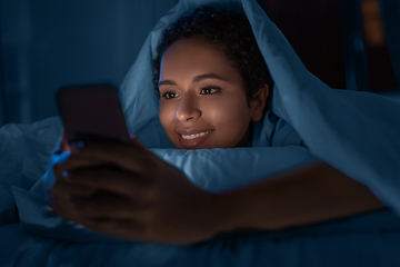 Image showing woman with smartphone under duvet in bed at night