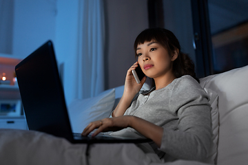 Image showing woman with laptop calling on phone in bed at night