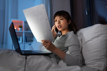 Image showing woman with laptop calling on phone in bed at night