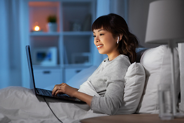 Image showing woman with laptop and earphones in bed at night