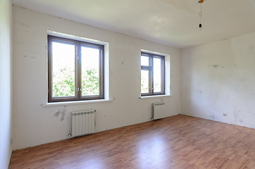 Image showing The interior of an empty room during renovation, there are two large windows in the room, radiators under them