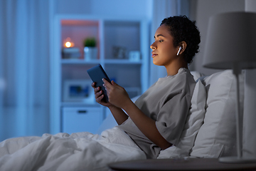 Image showing woman with tablet pc in earphones in bed at night