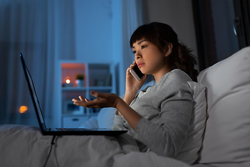 Image showing woman with laptop calling on phone in bed at night