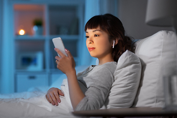 Image showing woman with phone and earphones in bed at night