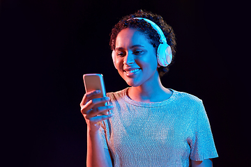 Image showing woman in headphones with smartphone in neon lights