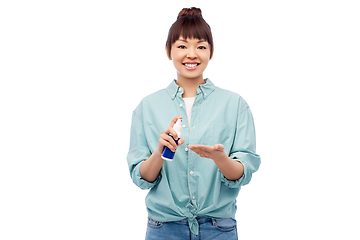 Image showing happy smiling asian woman using hand sanitizer