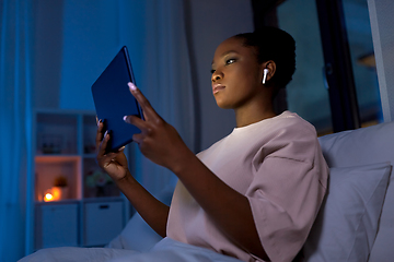 Image showing woman with tablet pc in earphones in bed at night