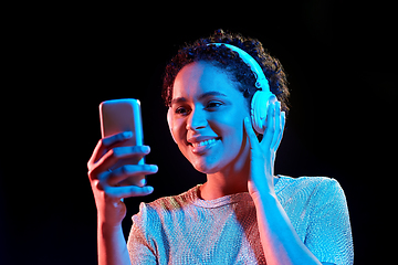 Image showing woman in headphones with smartphone in neon lights