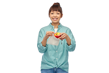 Image showing happy woman putting apple into reusable bag