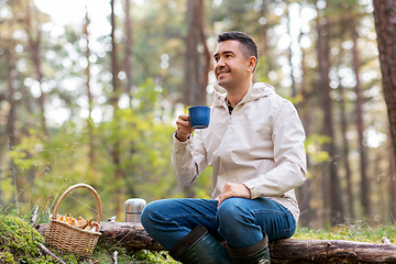 Image showing man with basket of mushrooms drinks tea in forest