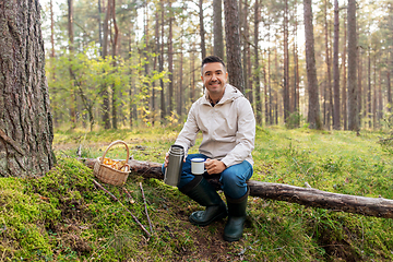 Image showing man with basket of mushrooms drinks tea in forest