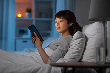 Image showing woman with tablet pc in earphones in bed at night