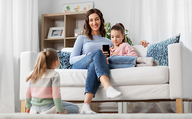 Image showing happy mother and daughters with smartphone at home