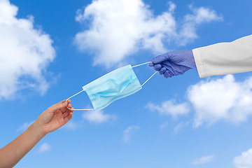 Image showing hand of doctor giving mask to patient over sky