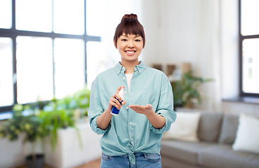 Image showing happy smiling asian woman using hand sanitizer