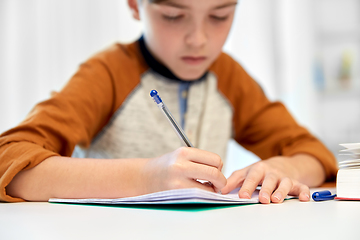 Image showing student boy with book writing to notebook at home