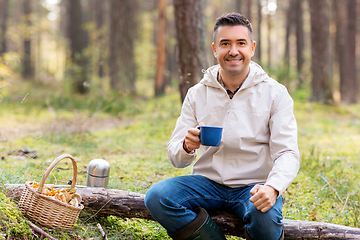 Image showing man with basket of mushrooms drinks tea in forest