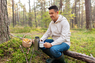 Image showing man with basket of mushrooms drinks tea in forest