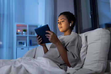 Image showing woman with tablet pc in earphones in bed at night