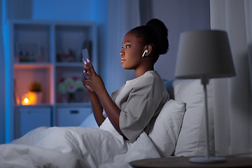 Image showing woman with smartphone and earbuds in bed at night