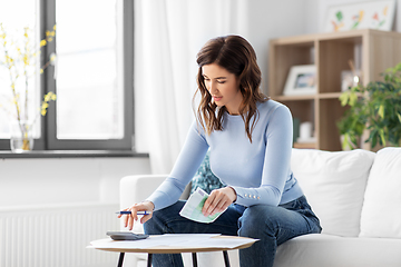 Image showing happy woman with calculator counting money at home