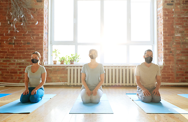 Image showing group of people in masks meditating at yoga studio